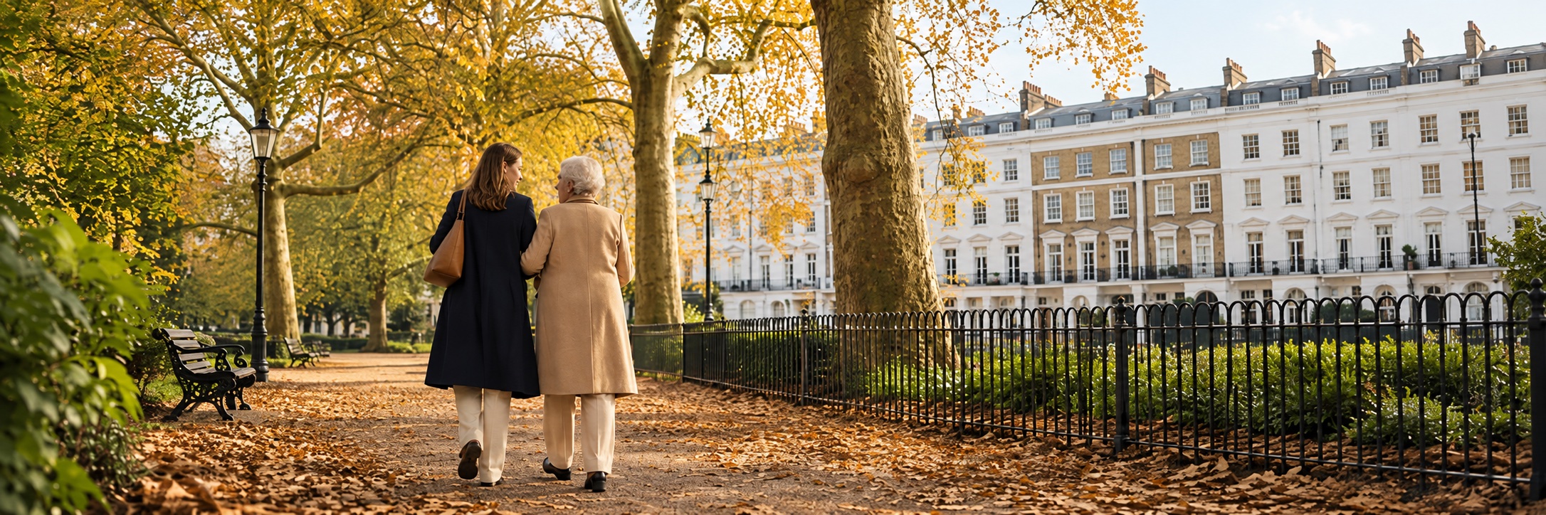 A carer and an older woman walking together through a leafy London square